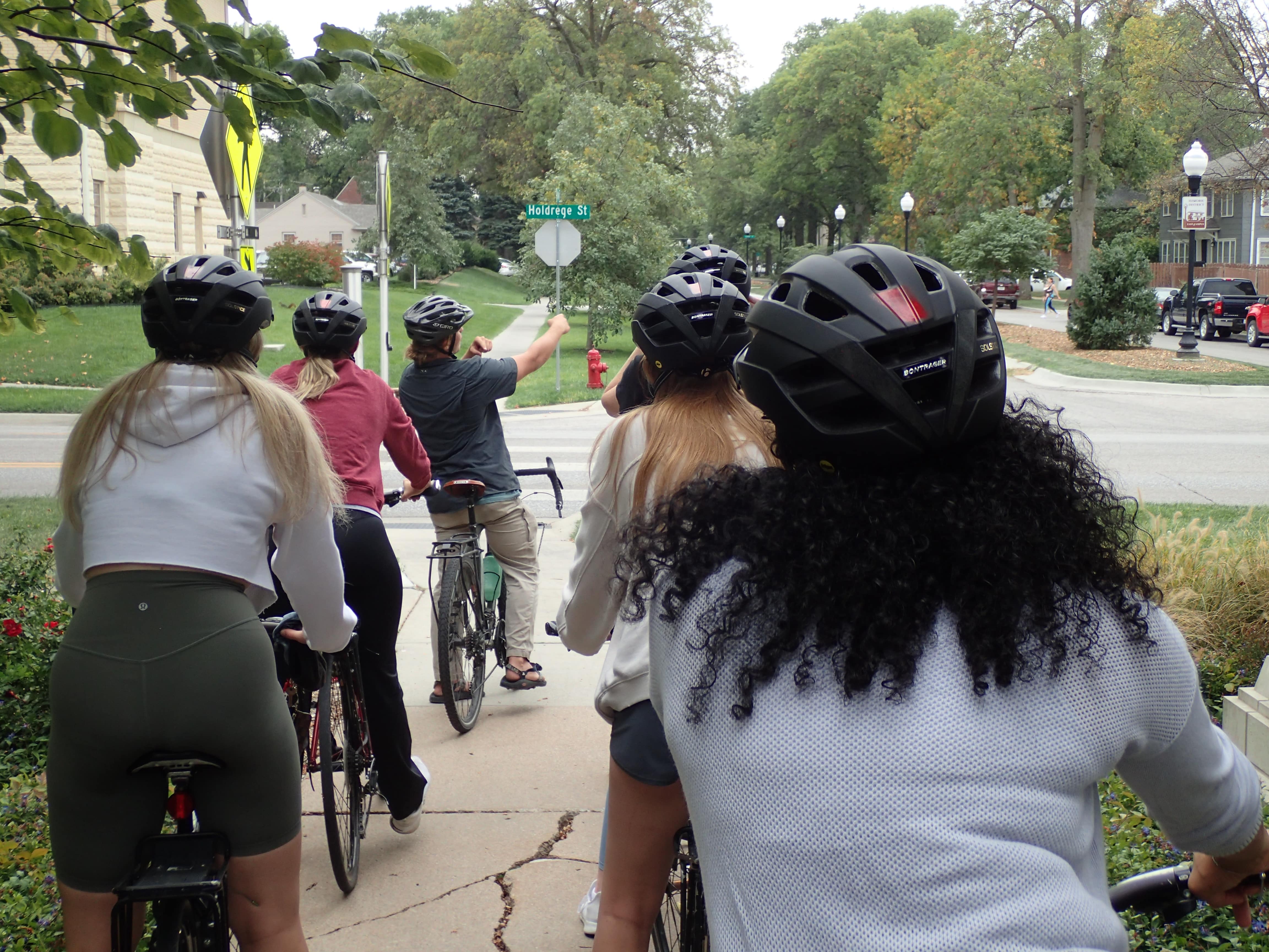 Students are seen from the back riding bikes on a city sidewalk