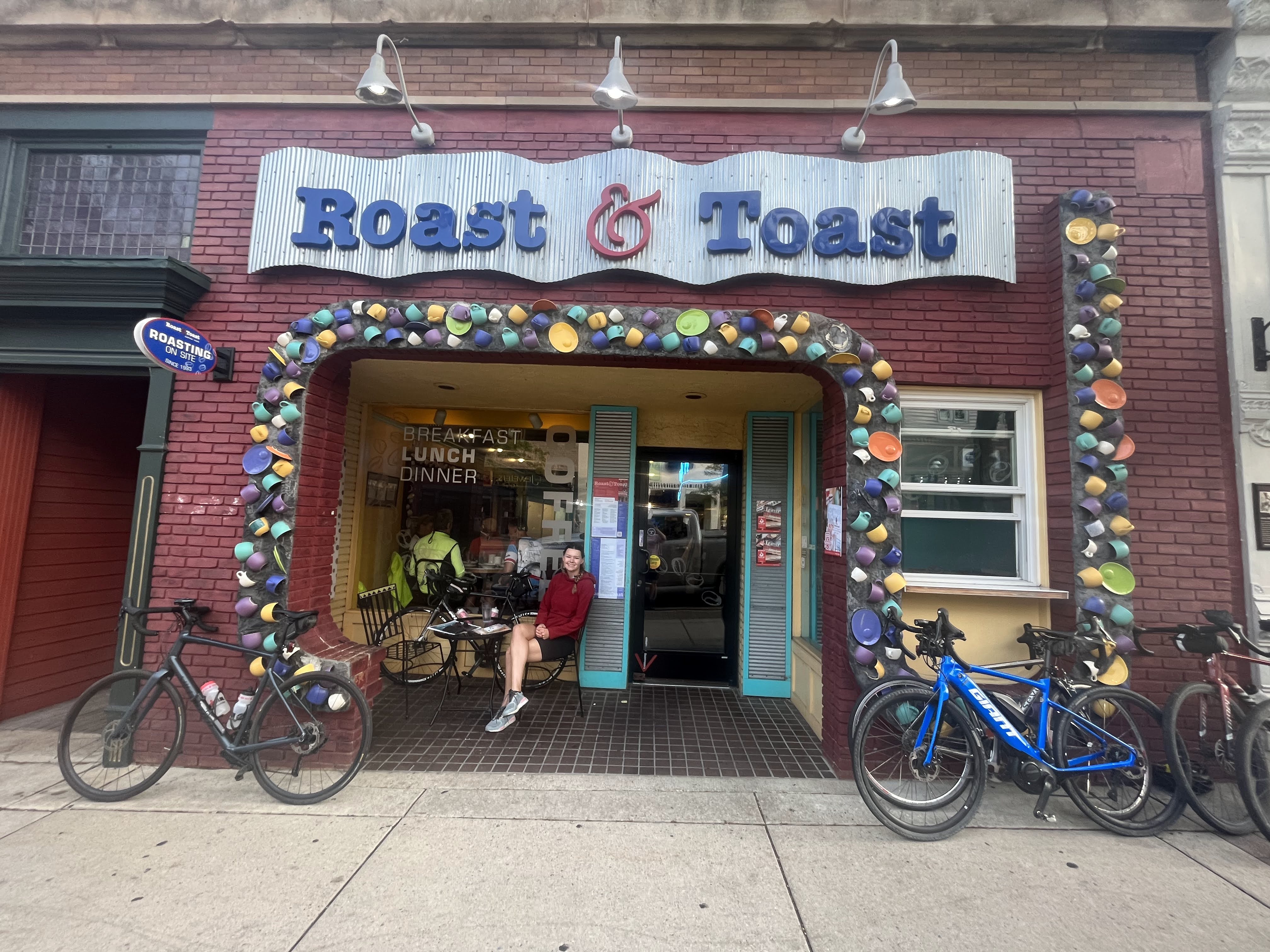 A young woman sits in front of Roast and Toast with bikes in the foreground of the photo