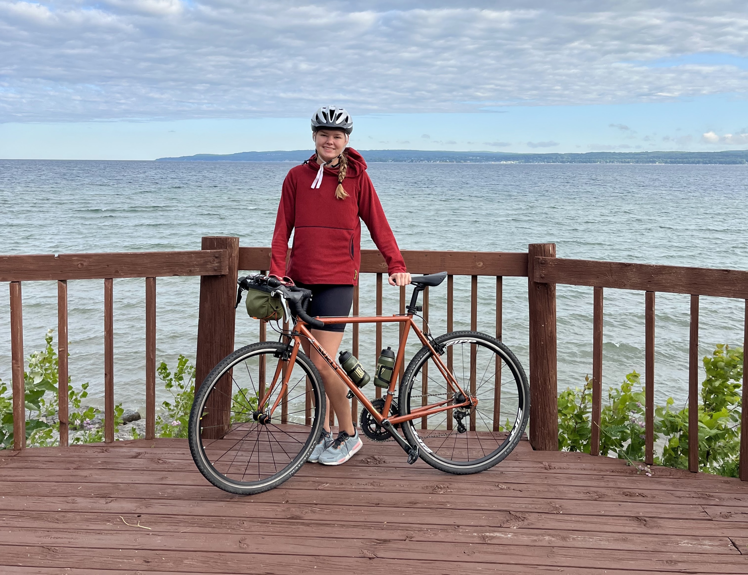 A young woman poses with her bike in front of a large body of water