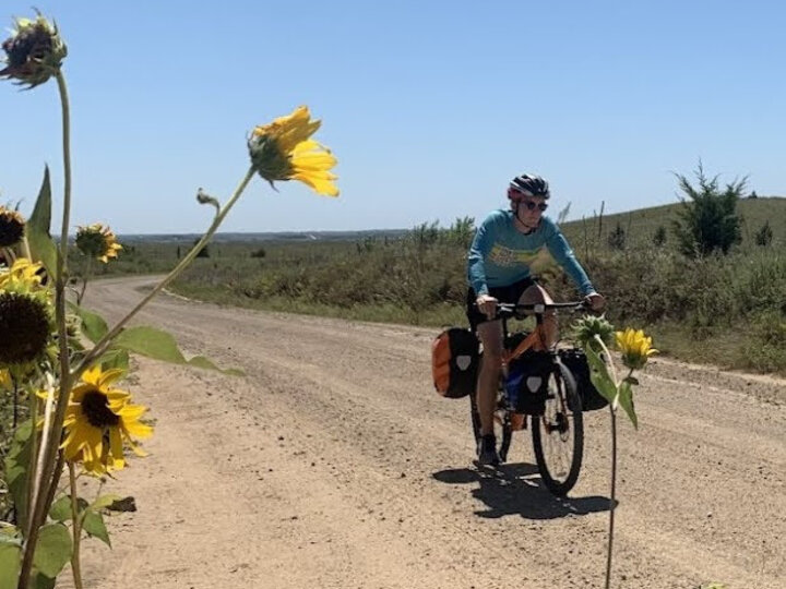 A cyclist riding on a dirt road with sunflowers in the foreground