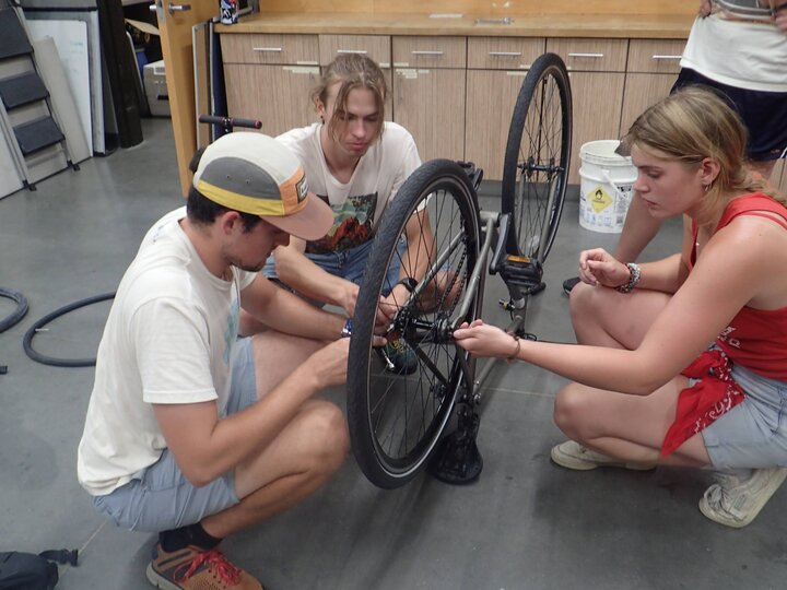 Three people repairing a bike that is flipped upside down